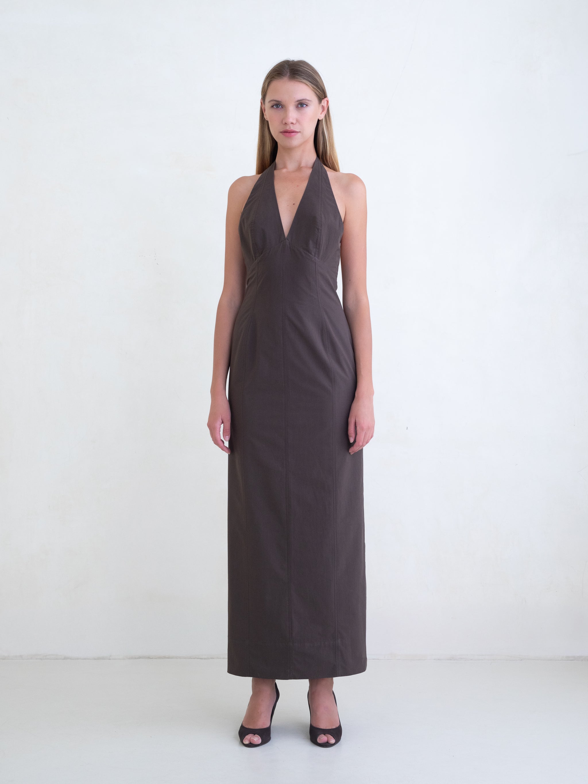 Woman wearing a brown sleeveless maxi dress with open low back on a white background. 