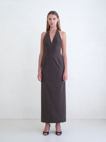 Woman wearing a brown sleeveless maxi dress with open low back on a white background. 