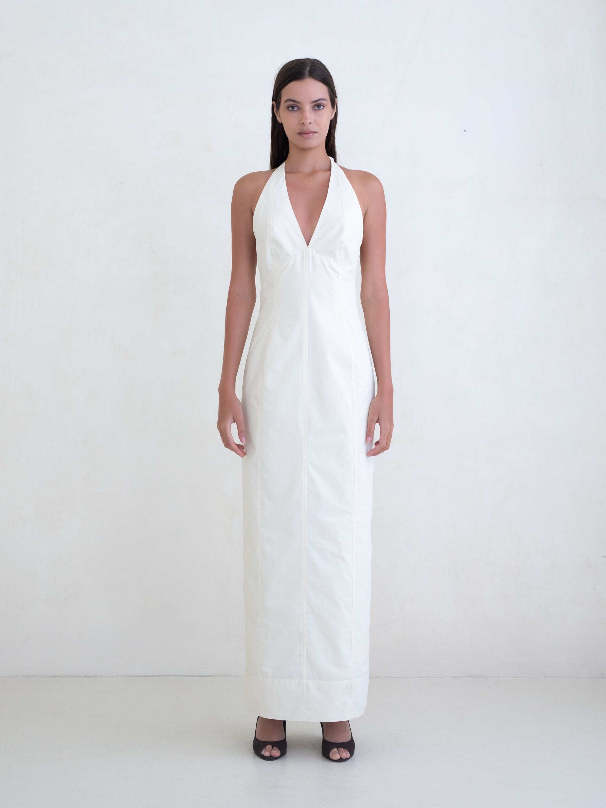 Woman wearing a cream sleeveless maxi dress with open low back on a white background. 