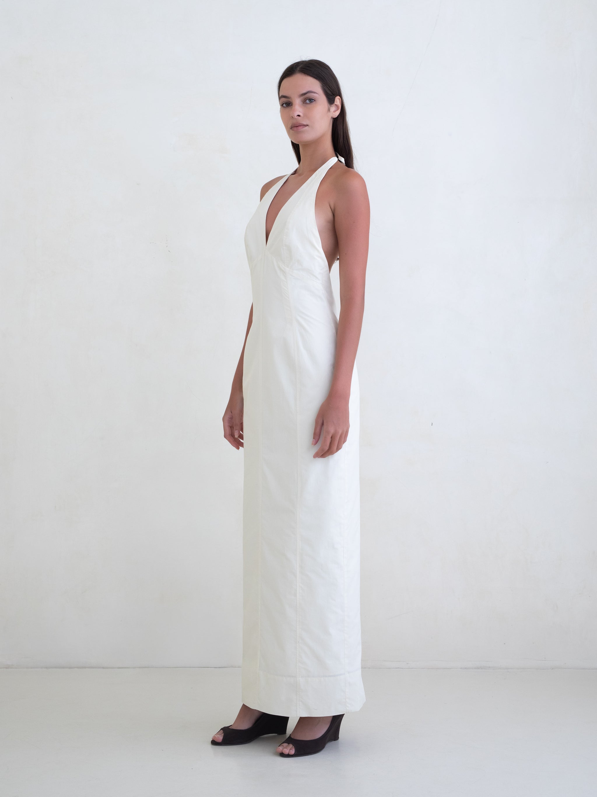 Woman wearing a cream sleeveless maxi dress with open low back on a white background. 