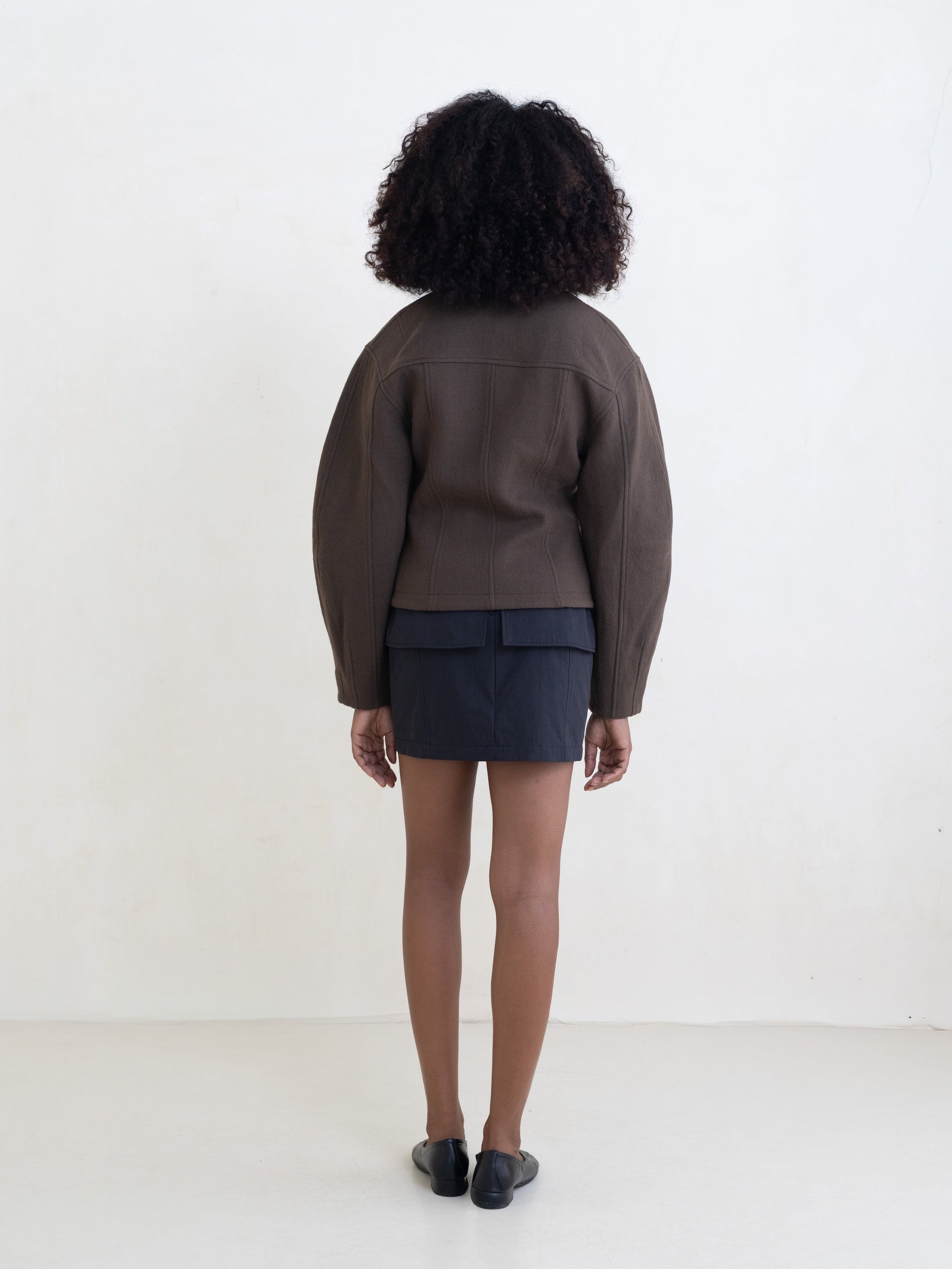 Woman wearing a brown zip-front jacket and a black mini skirt on a white background. 