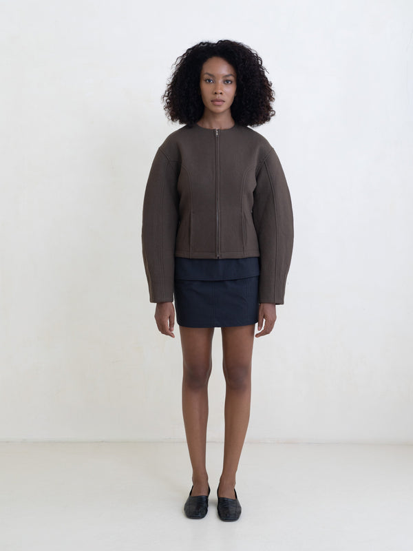 Woman wearing a brown zip-front jacket and a black mini skirt on a white background. 
