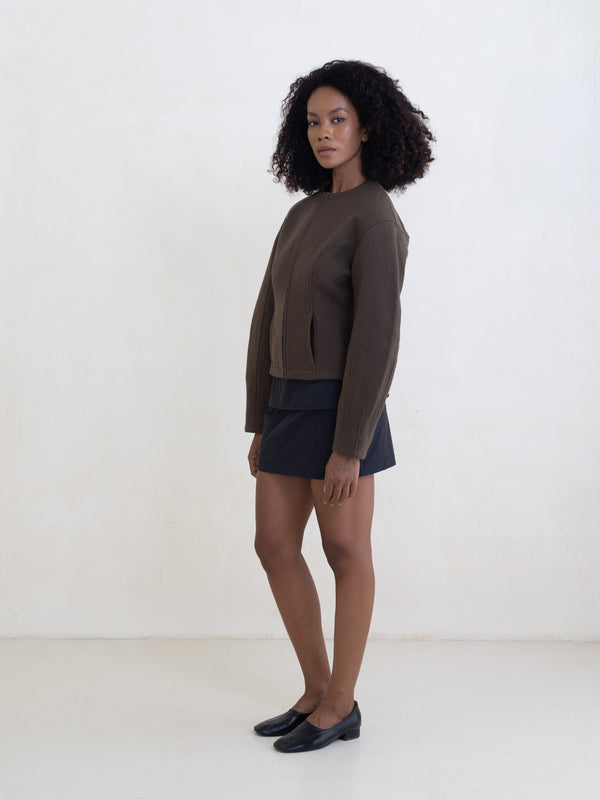Woman wearing a brown zip-front jacket and a black mini skirt on a white background. 