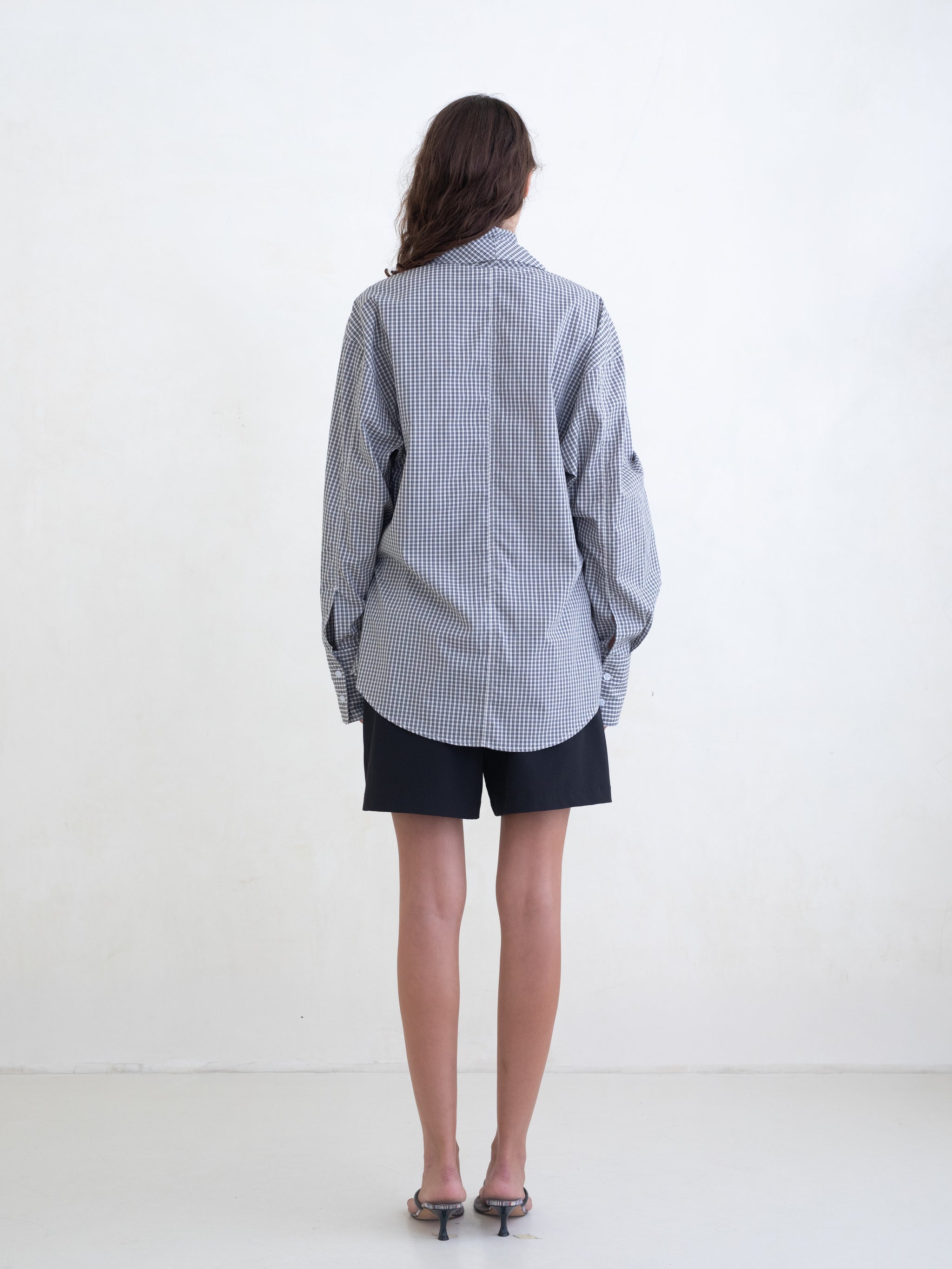 Woman wearing a black plaid wrap shirt and black shorts on a white background.  