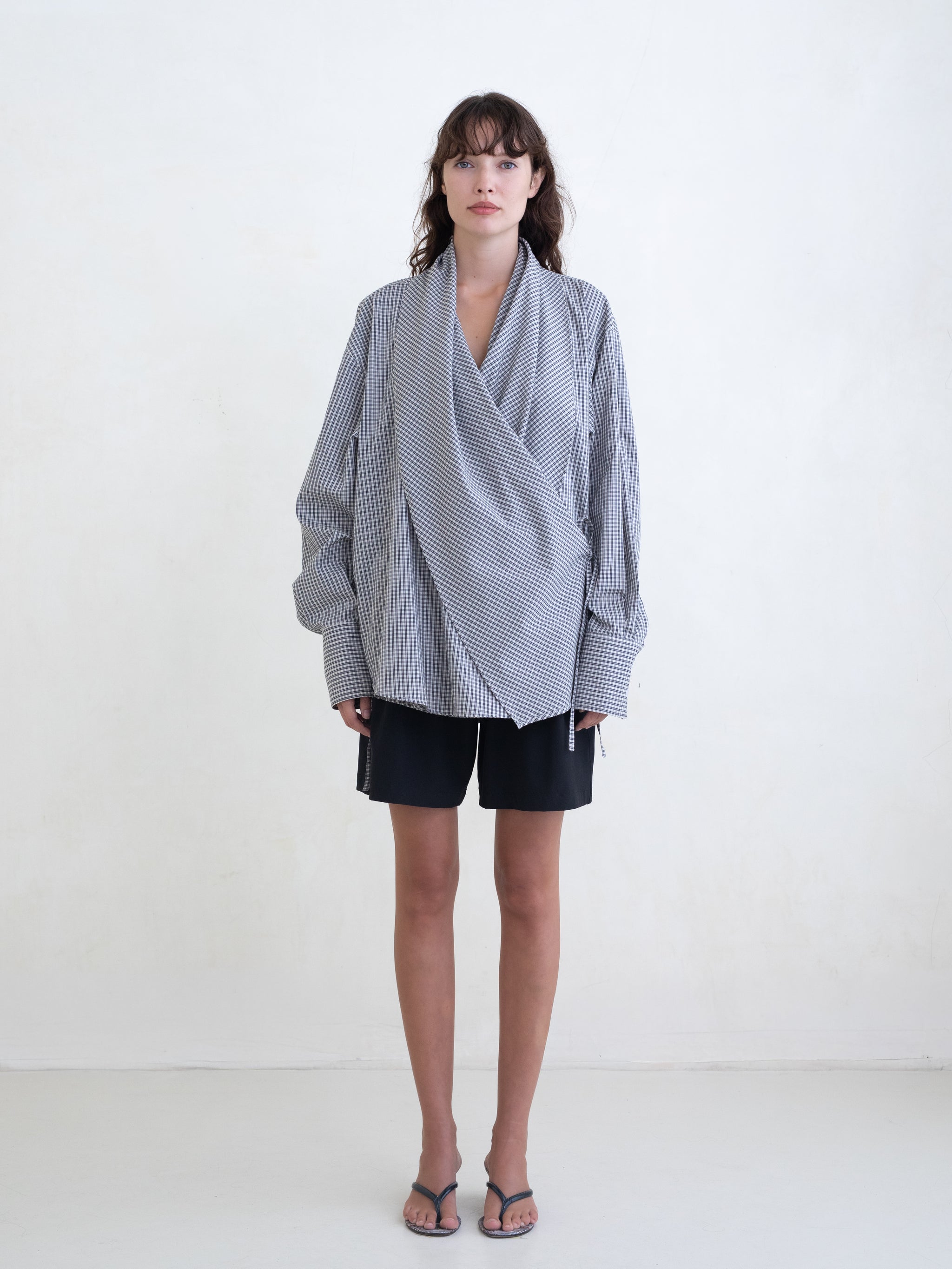 Woman wearing a black plaid wrap shirt and black shorts on a white background.  