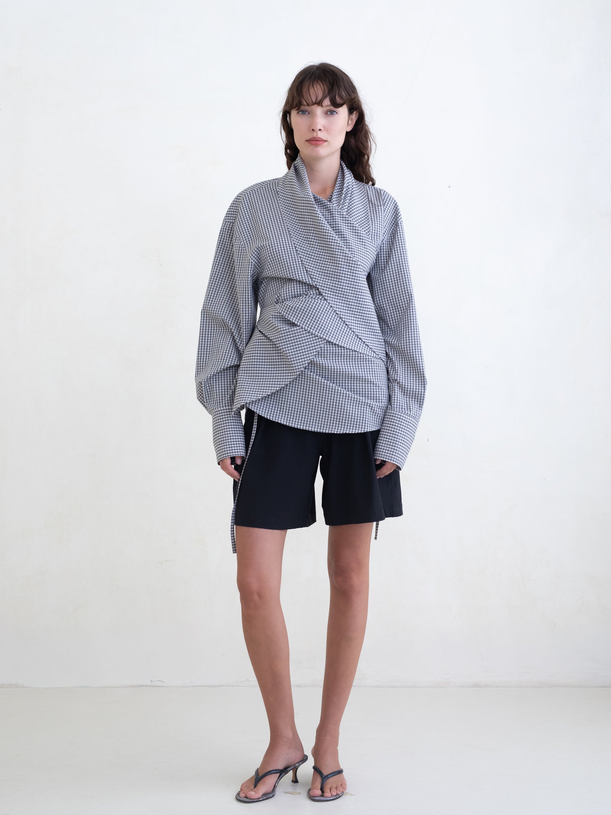 Woman wearing a black plaid wrap shirt and black shorts on a white background.  