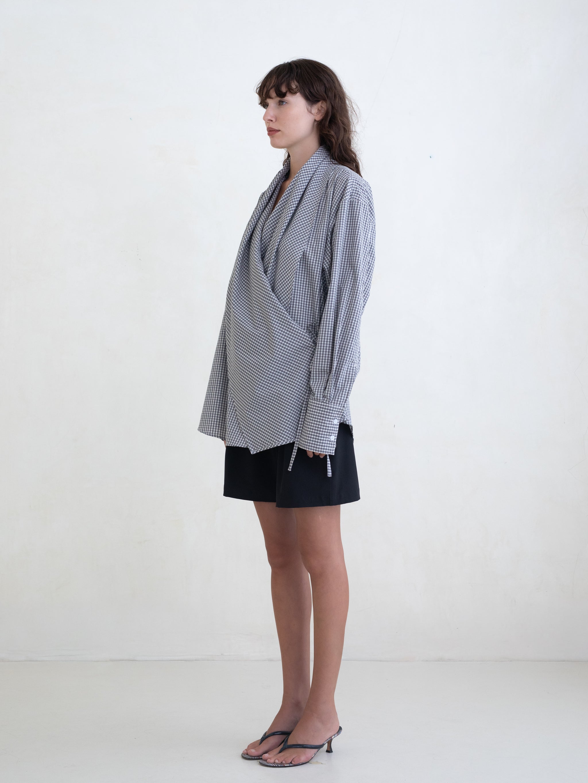 Woman wearing a black plaid wrap shirt and black shorts on a white background.  