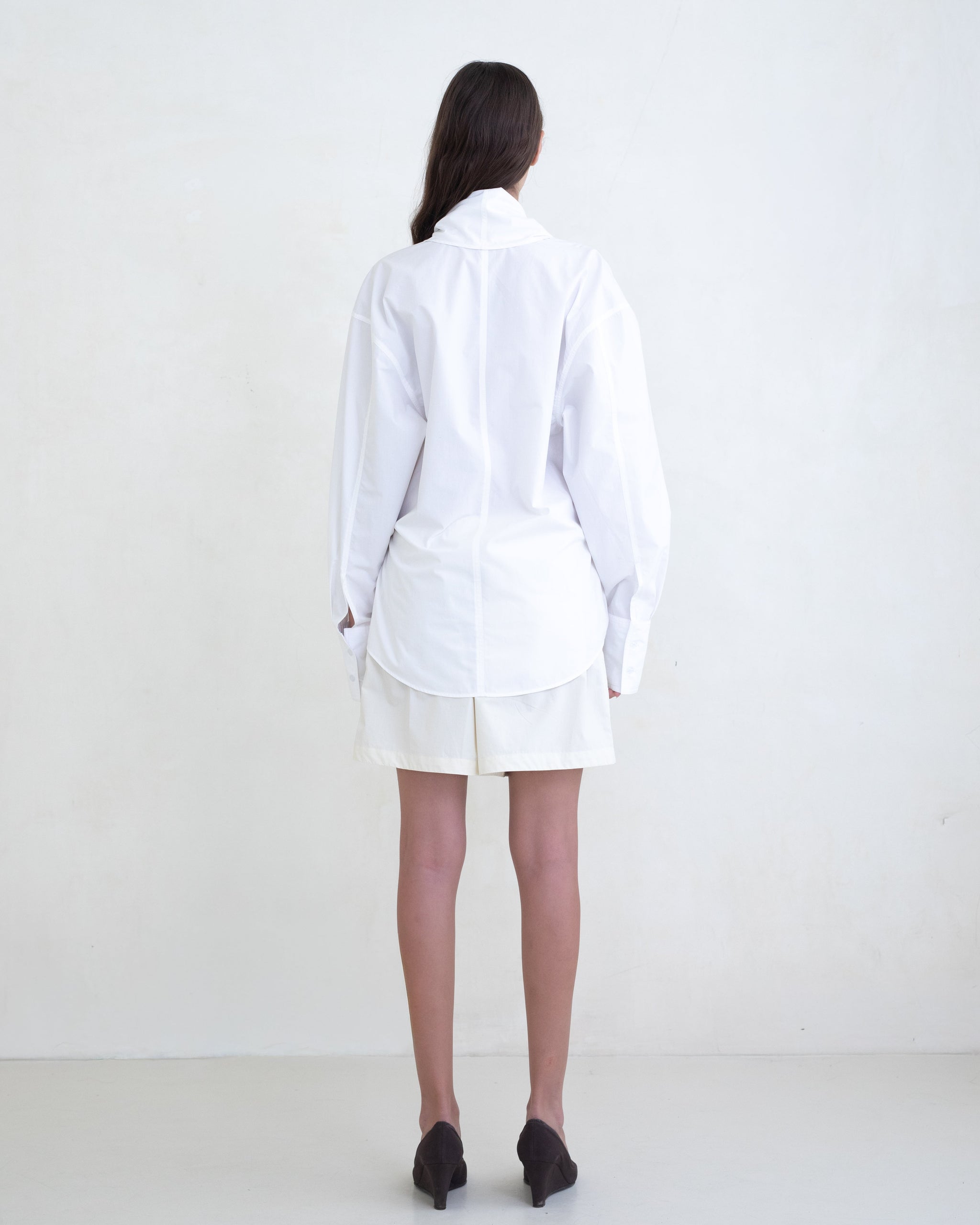 Woman wearing a white wrap shirt and cream shorts on a white background. 