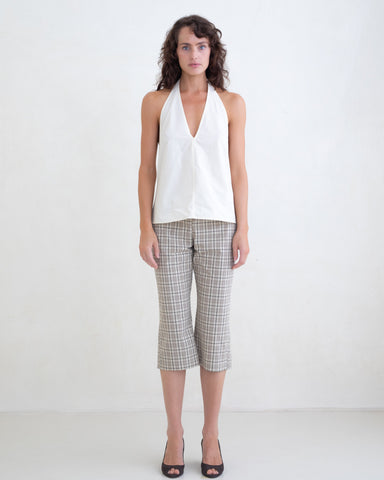 Woman wearing a cream v-neck halter top and brown plaid capri pants on a white background. 