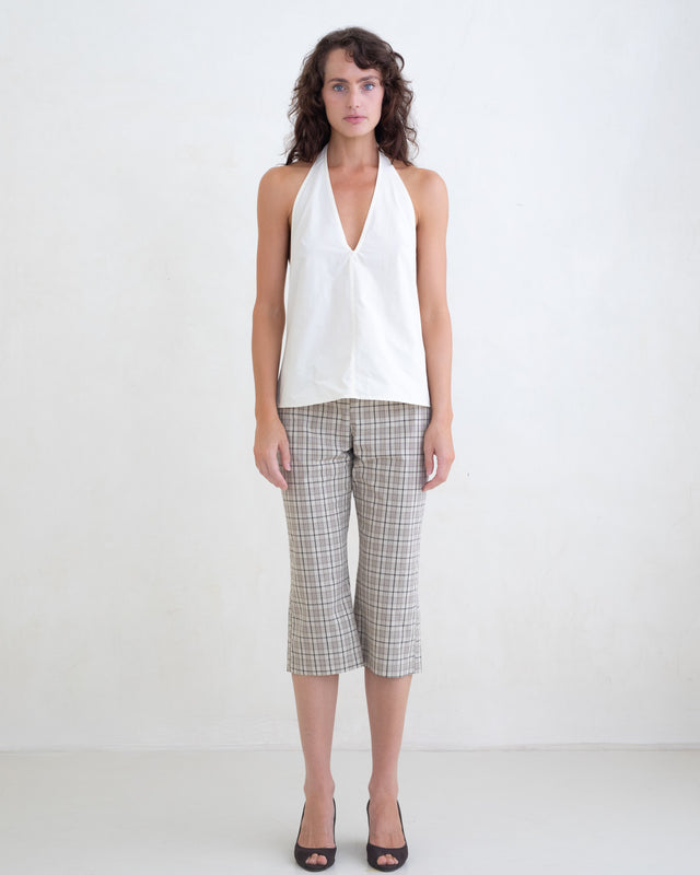Woman wearing a cream v-neck halter top and brown plaid capri pants on a white background. 