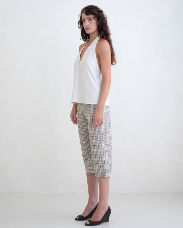 Woman wearing a cream v-neck halter top and brown plaid capri pants on a white background. 