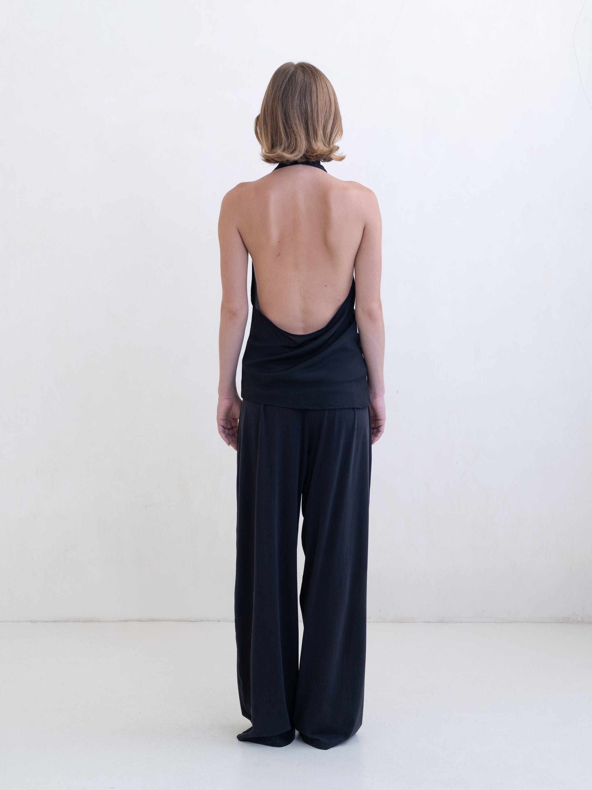 Woman wearing a black asymmetric halter-neck top and black pants on a white background. 