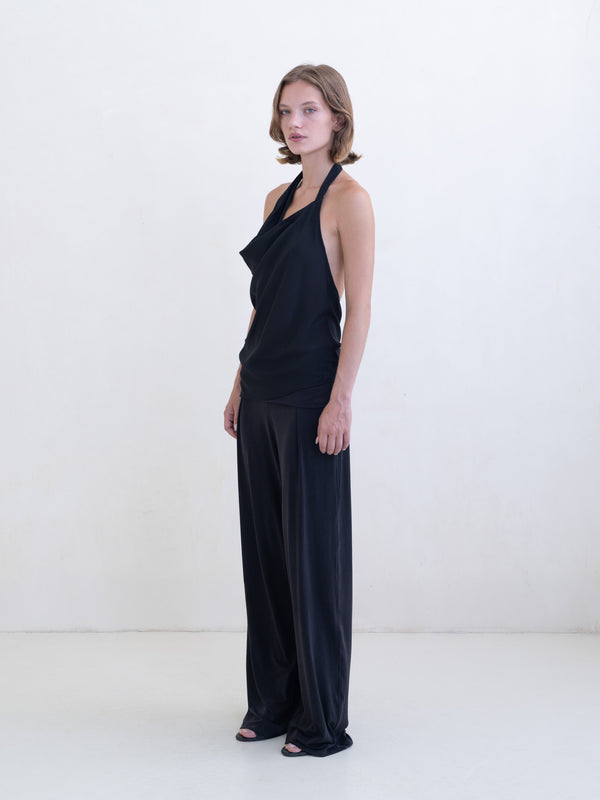 Woman wearing a black asymmetric halter-neck top and black pants on a white background. 