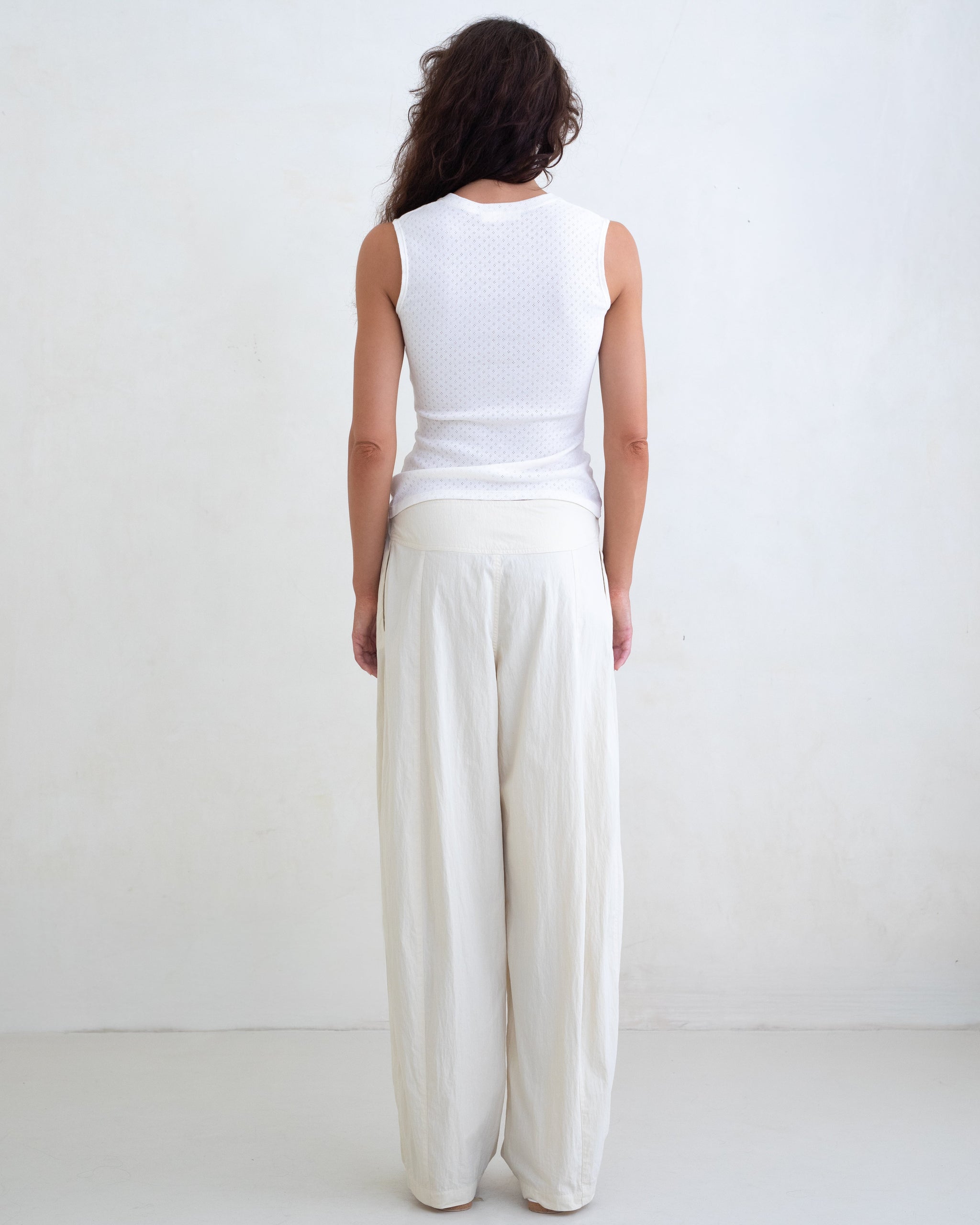 Woman wearing a white V-neck top and cream straight leg pants on a white background. 