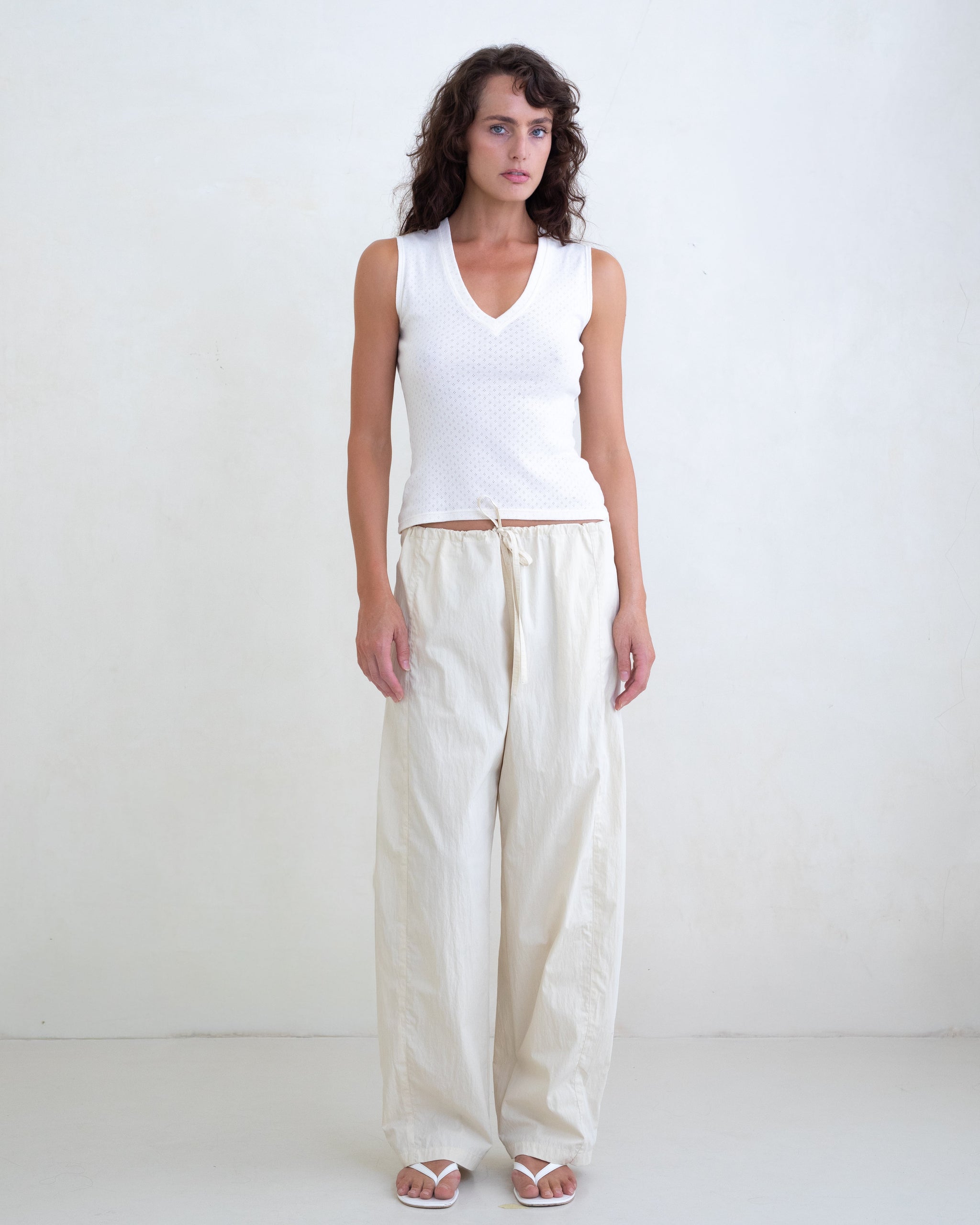 Woman wearing a white V-neck top and cream straight leg pants on a white background. 