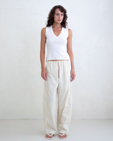 Woman wearing a white V-neck top and cream straight leg pants on a white background. 