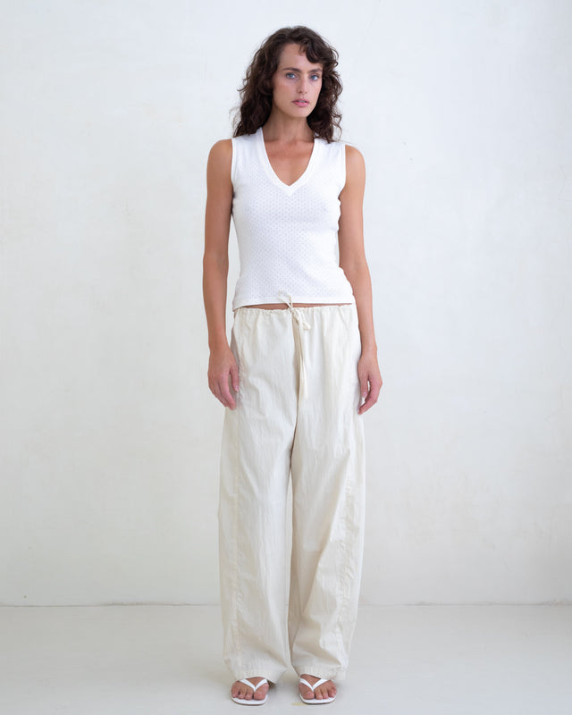 Woman wearing a white V-neck top and cream straight leg pants on a white background. 