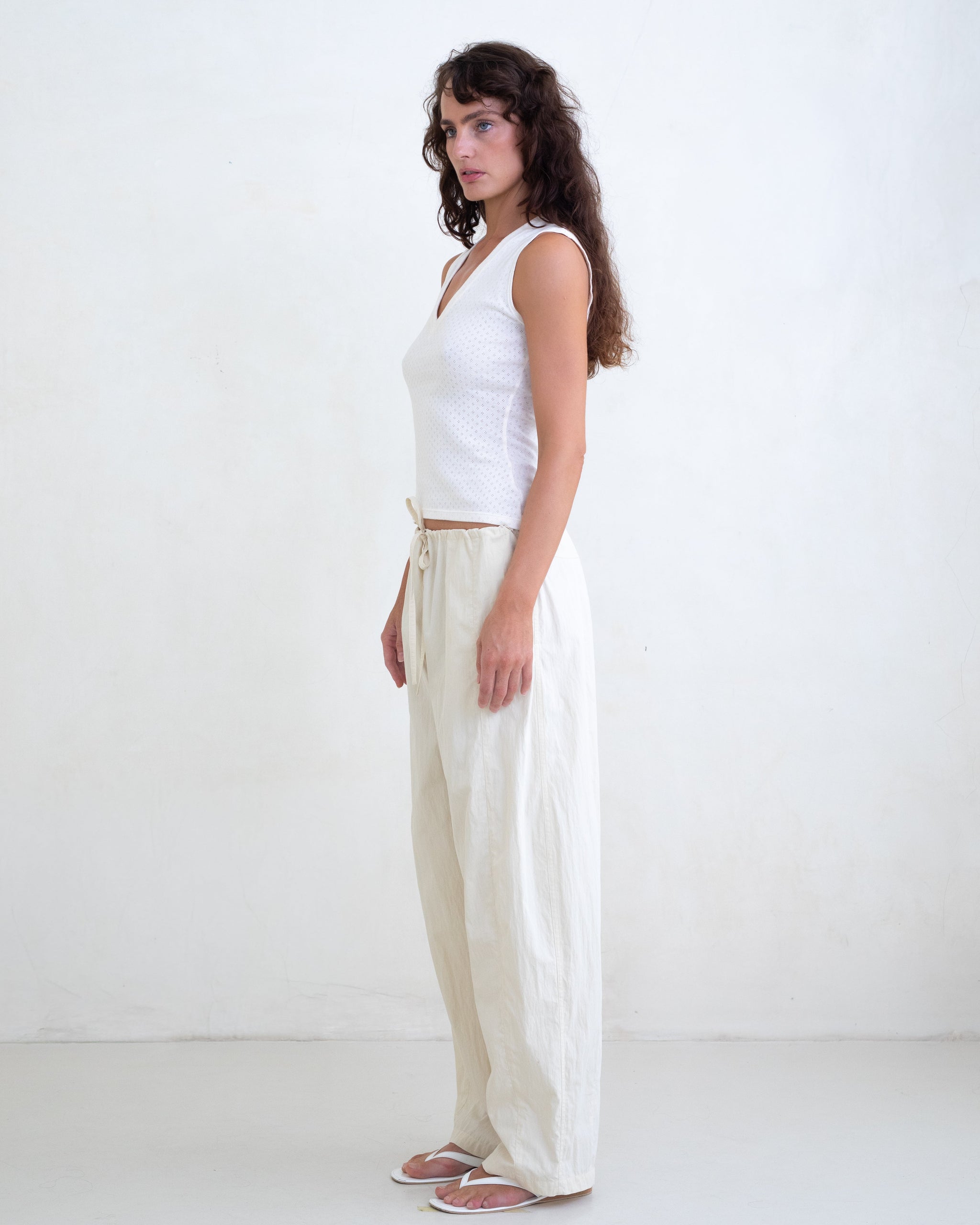 Woman wearing a white V-neck top and cream straight leg pants on a white background. 
