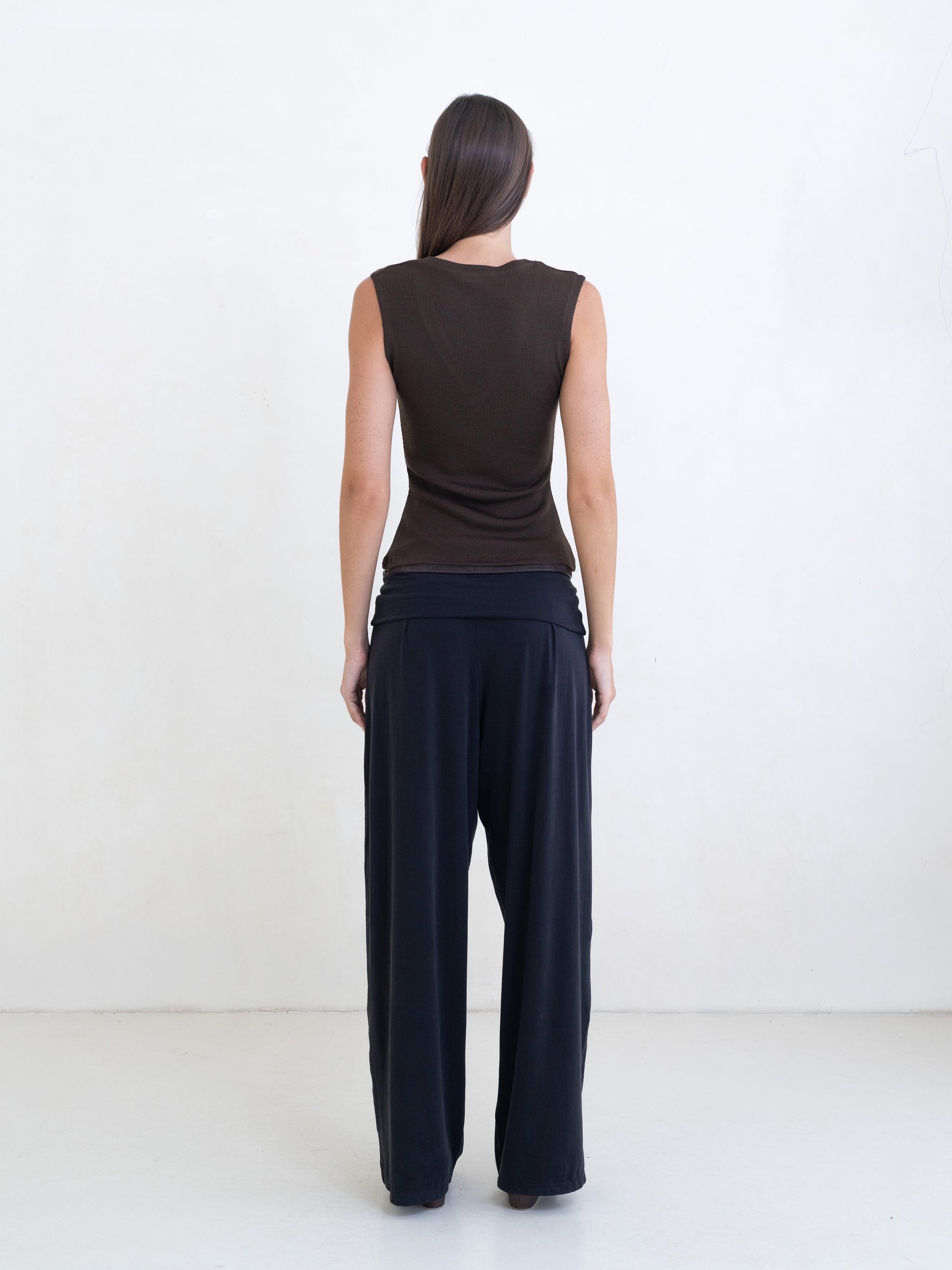 Woman wearing a brown sleeveless v-neck top and black pants on a white background. 