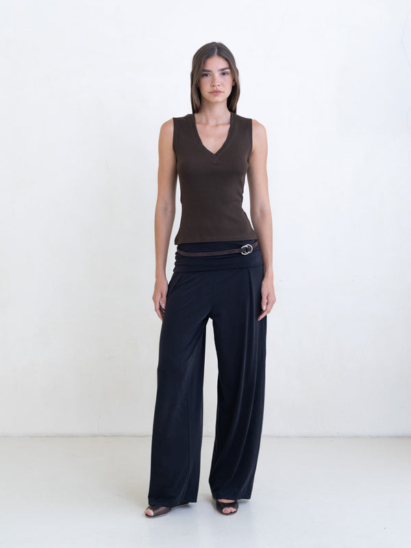 Woman wearing a brown sleeveless v-neck top and black pants on a white background. 