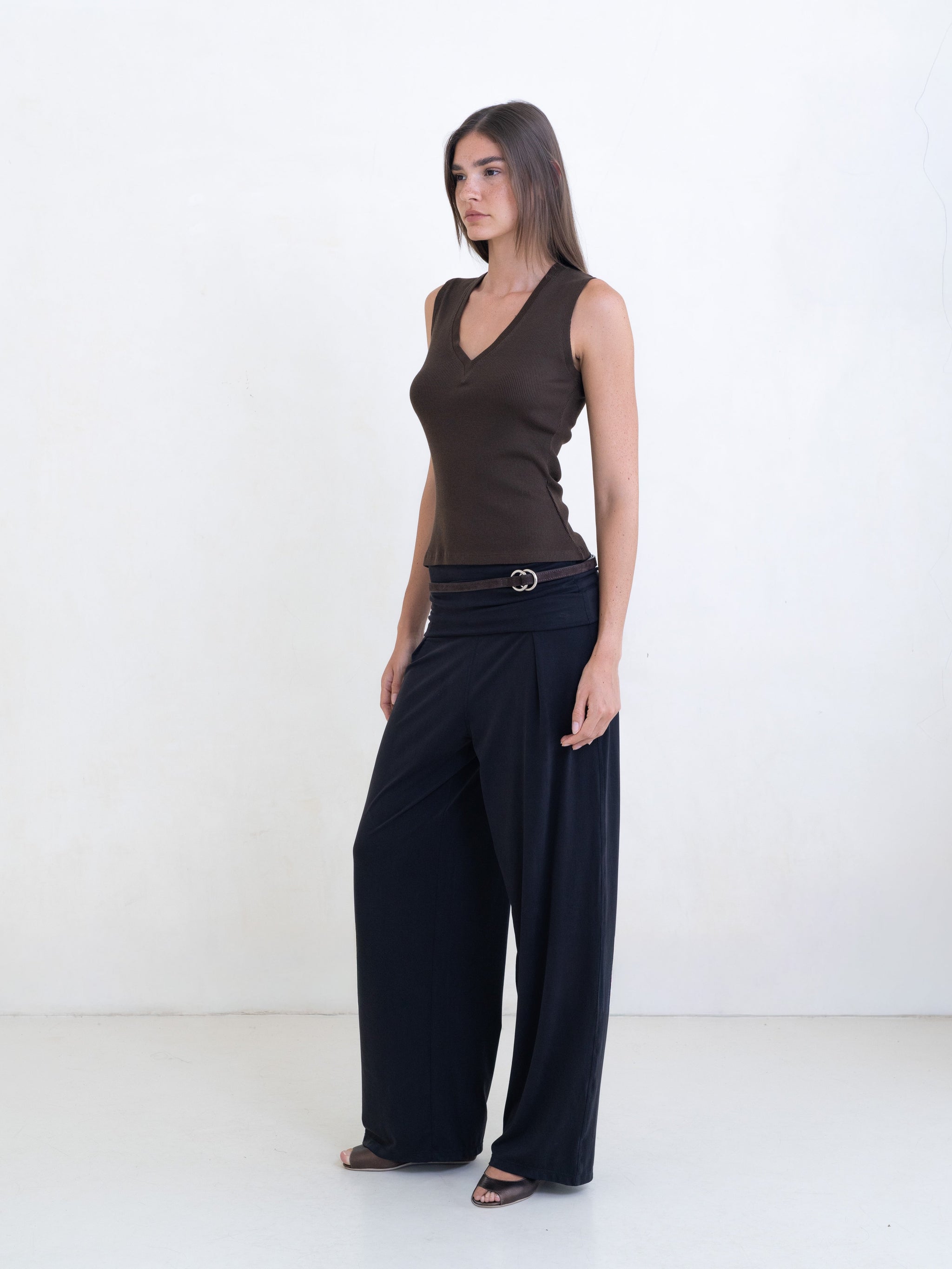 Woman wearing a brown sleeveless v-neck top and black pants on a white background. 