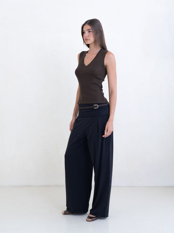 Woman wearing a brown sleeveless v-neck top and black pants on a white background. 