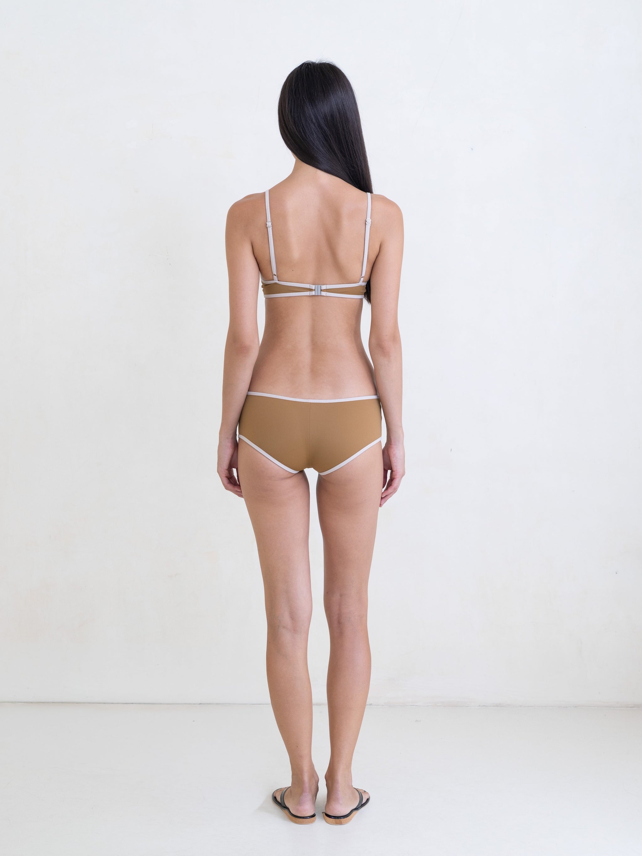Woman wearing a golden brown bikini with a contrast white trim on a white background