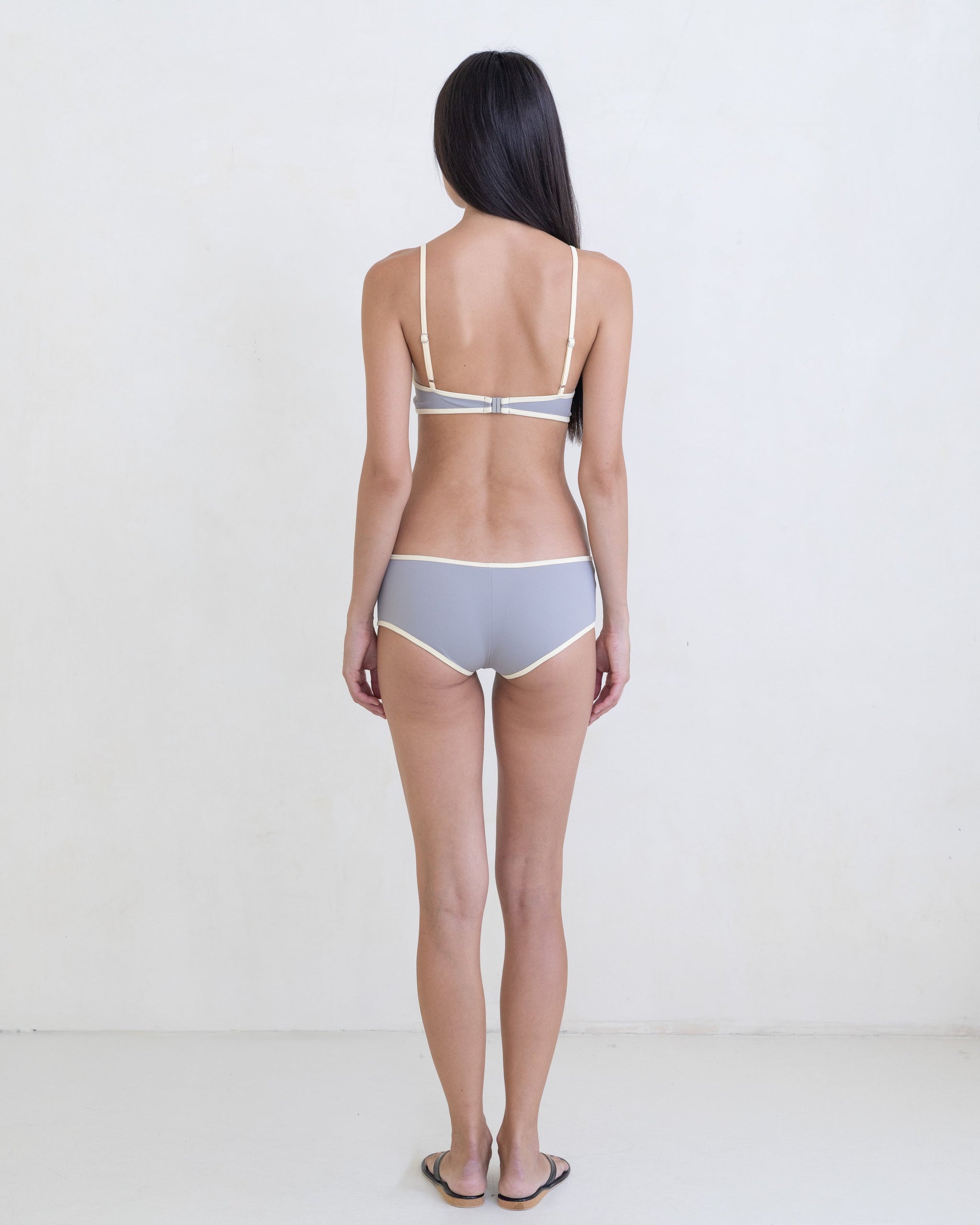 Woman wearing a dark gray bikini with a contrast white trim on a white background.