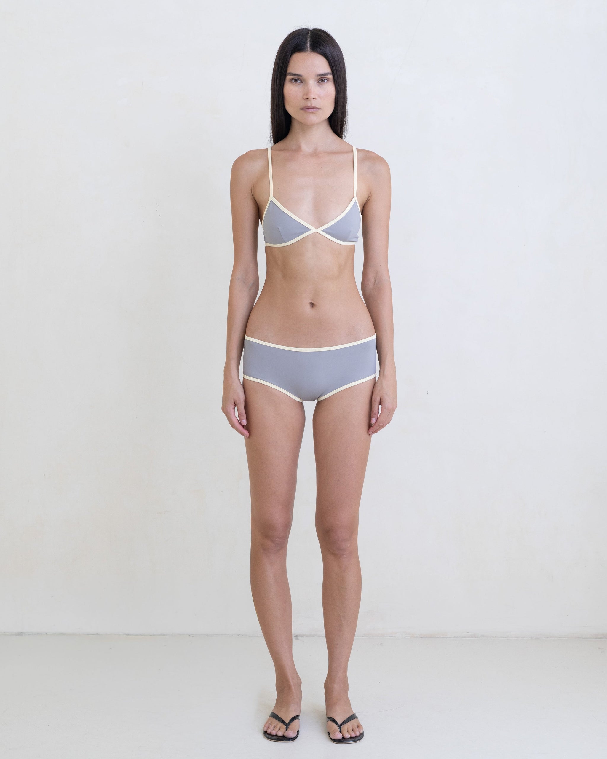 Woman wearing a dark gray bikini with a contrast white trim on a white background.
