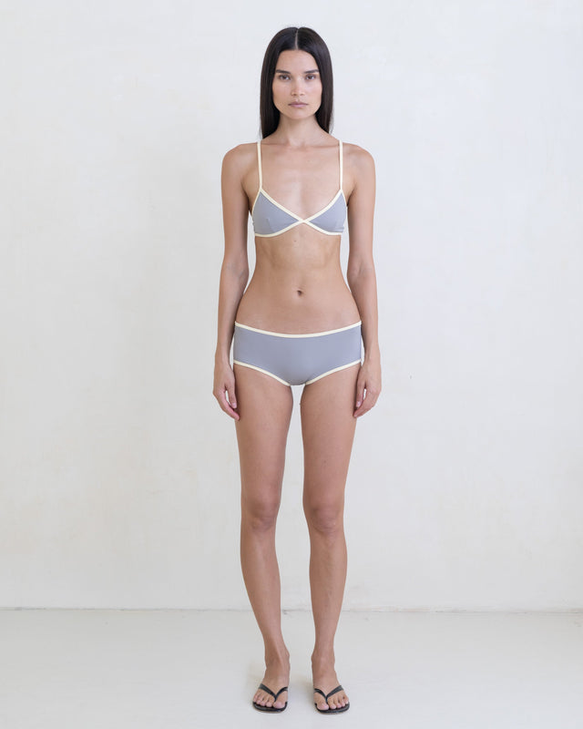 Woman wearing a dark gray bikini with a contrast white trim on a white background.