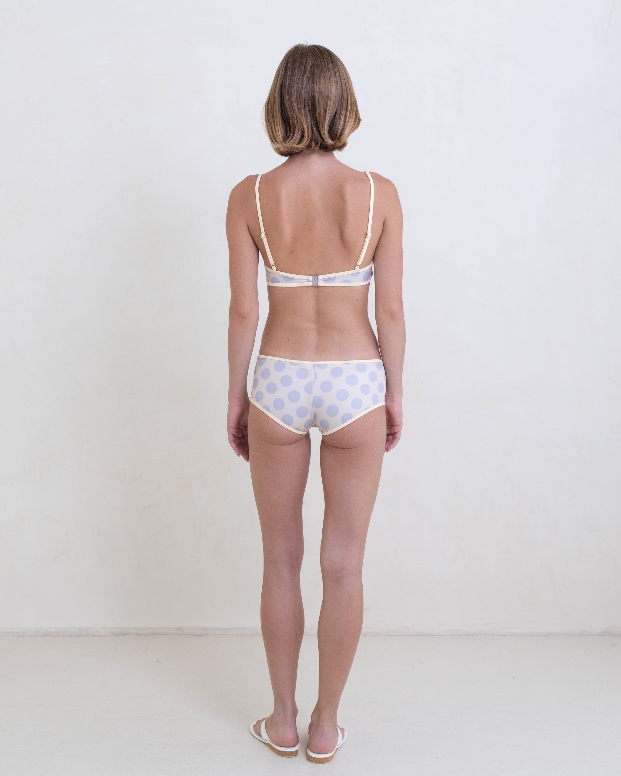Woman wearing a gray polka dot bikini with a contrast white trim on a white background.