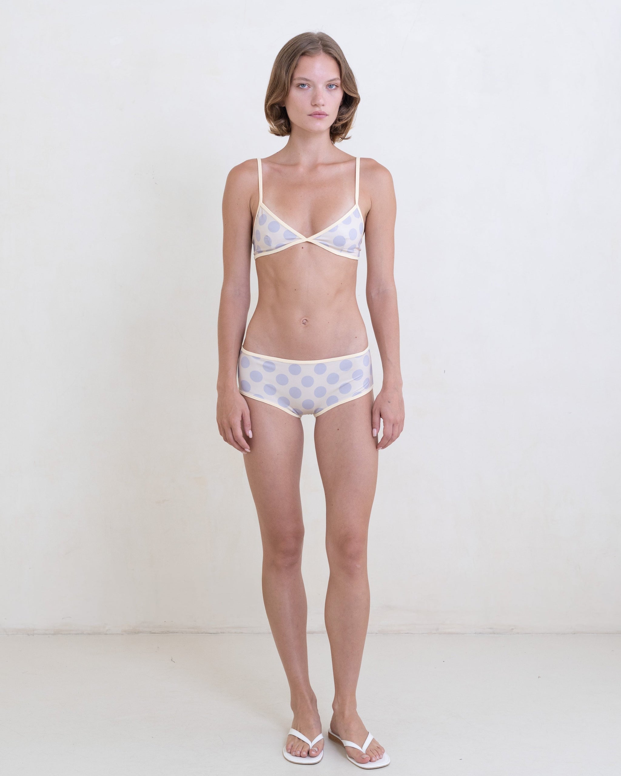 Woman wearing a gray polka dot bikini with a contrast white trim on a white background.