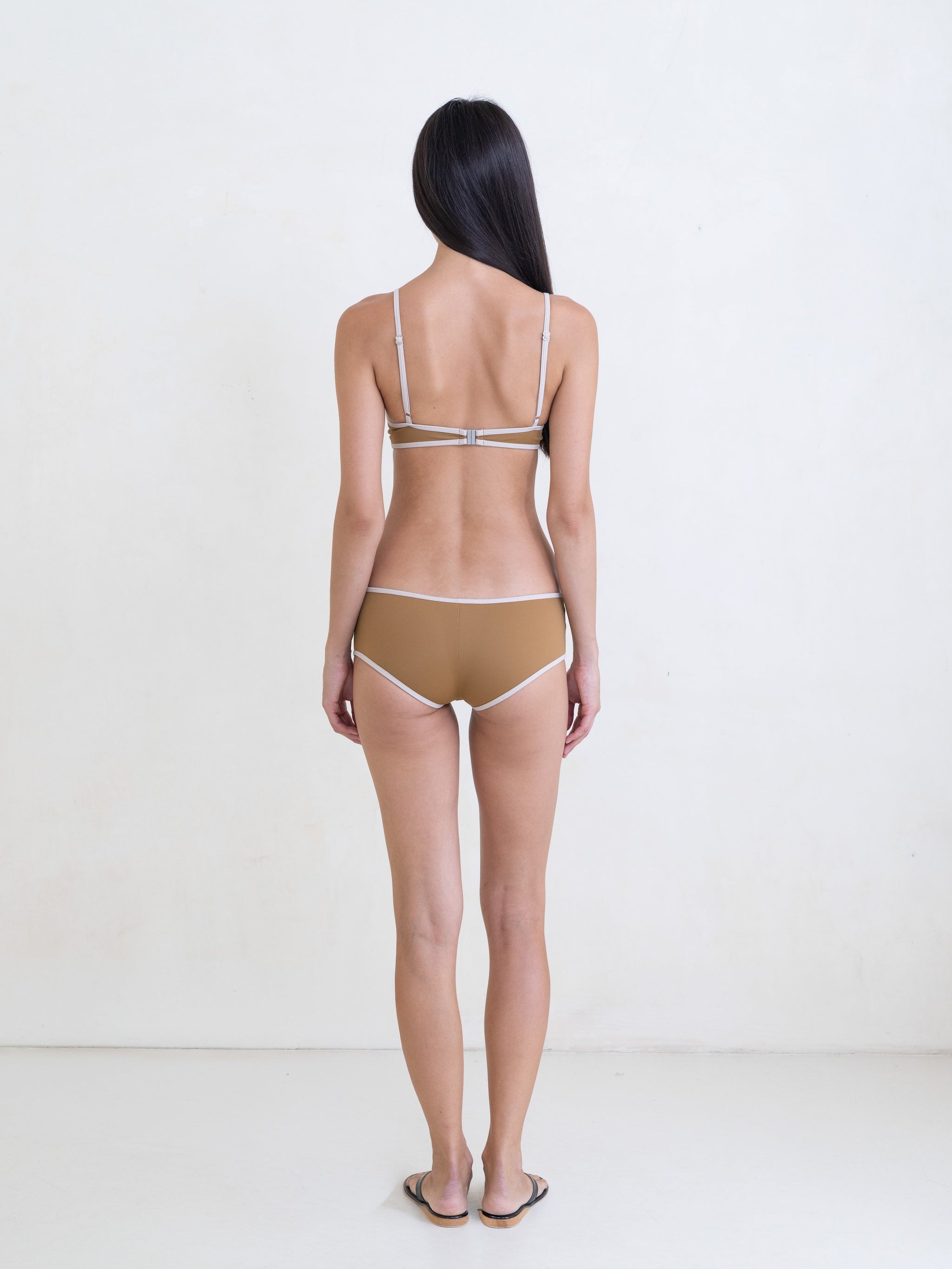 Woman wearing a golden brown bikini with a contrast white trim on a white background