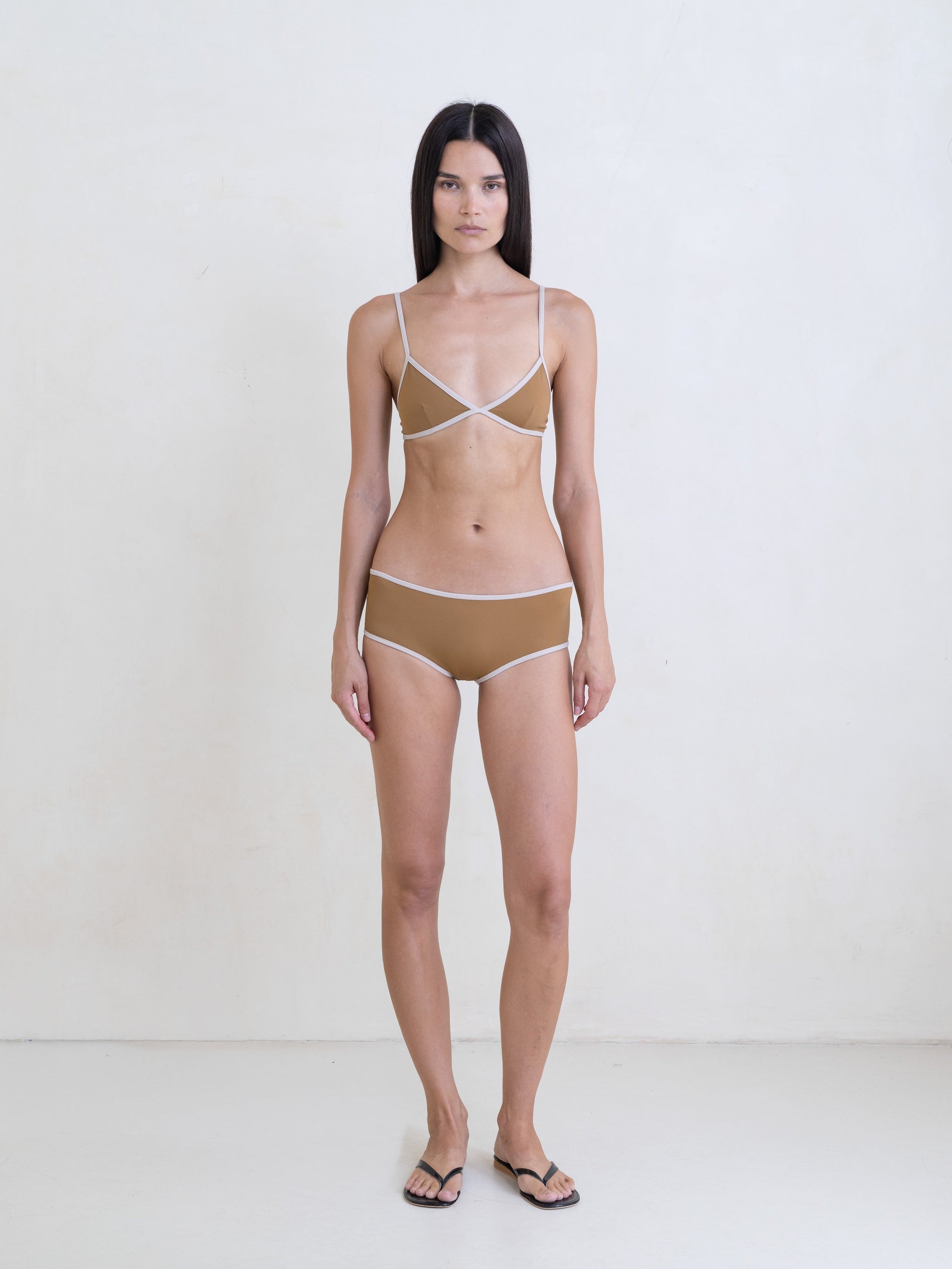 Woman wearing a golden brown bikini with a contrast white trim on a white background