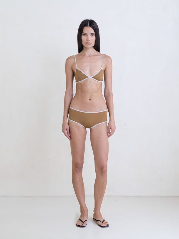 Woman wearing a golden brown bikini with a contrast white trim on a white background
