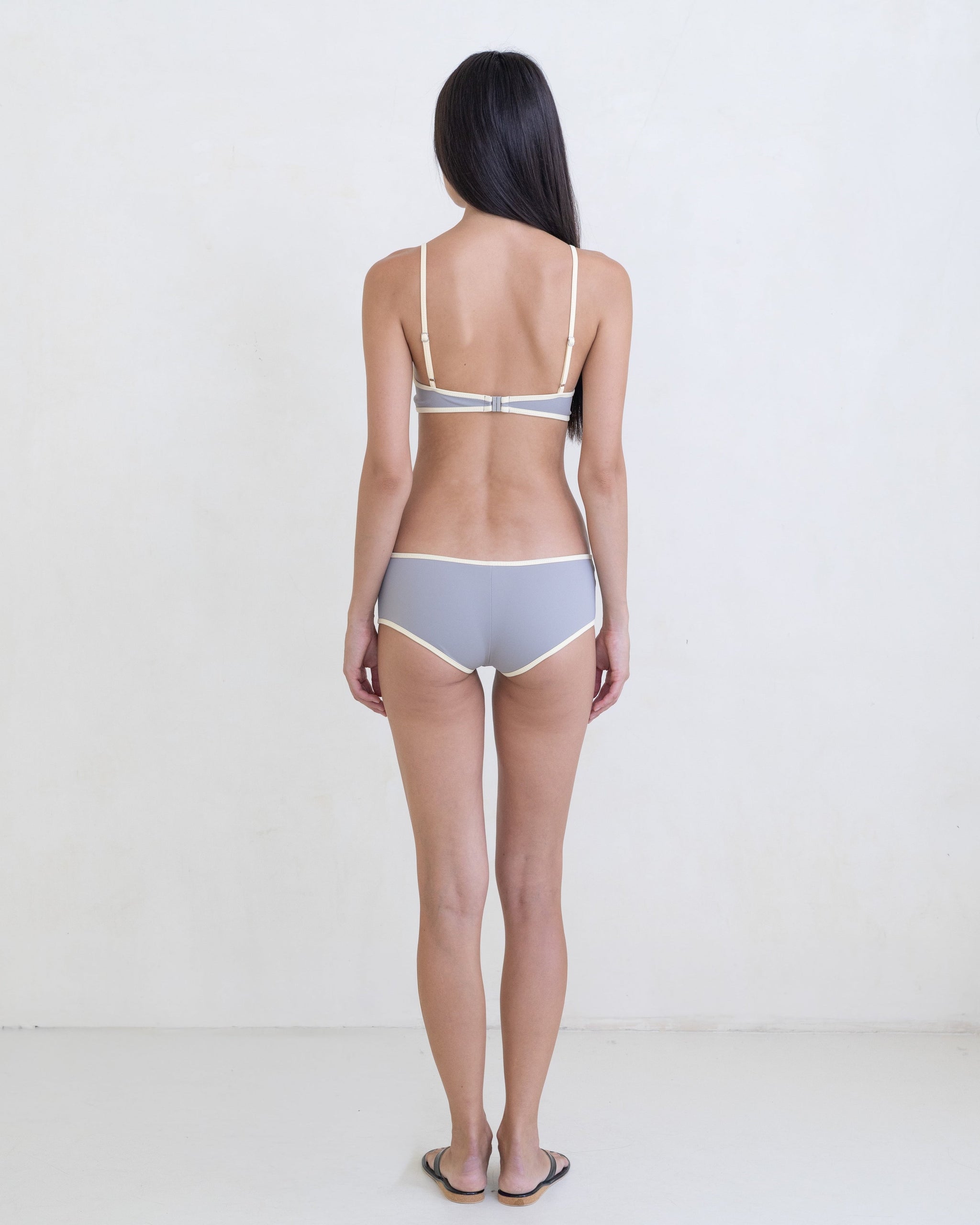 Woman wearing a dark gray bikini with a contrast white trim on a white background.