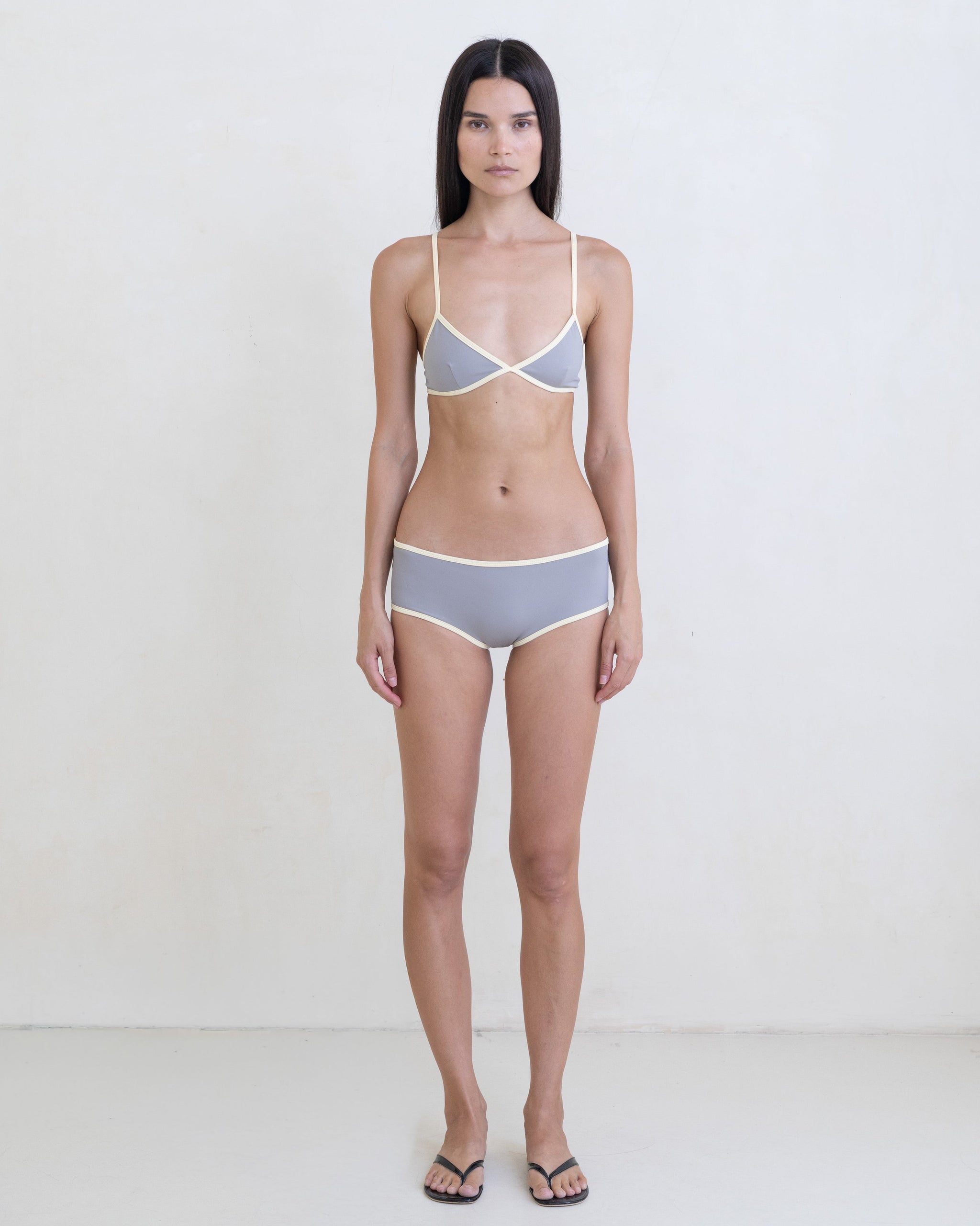 Woman wearing a dark gray bikini with a contrast white trim on a white background.