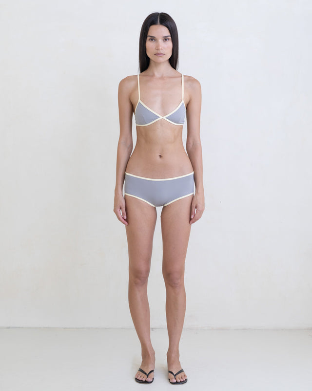 Woman wearing a dark gray bikini with a contrast white trim on a white background.