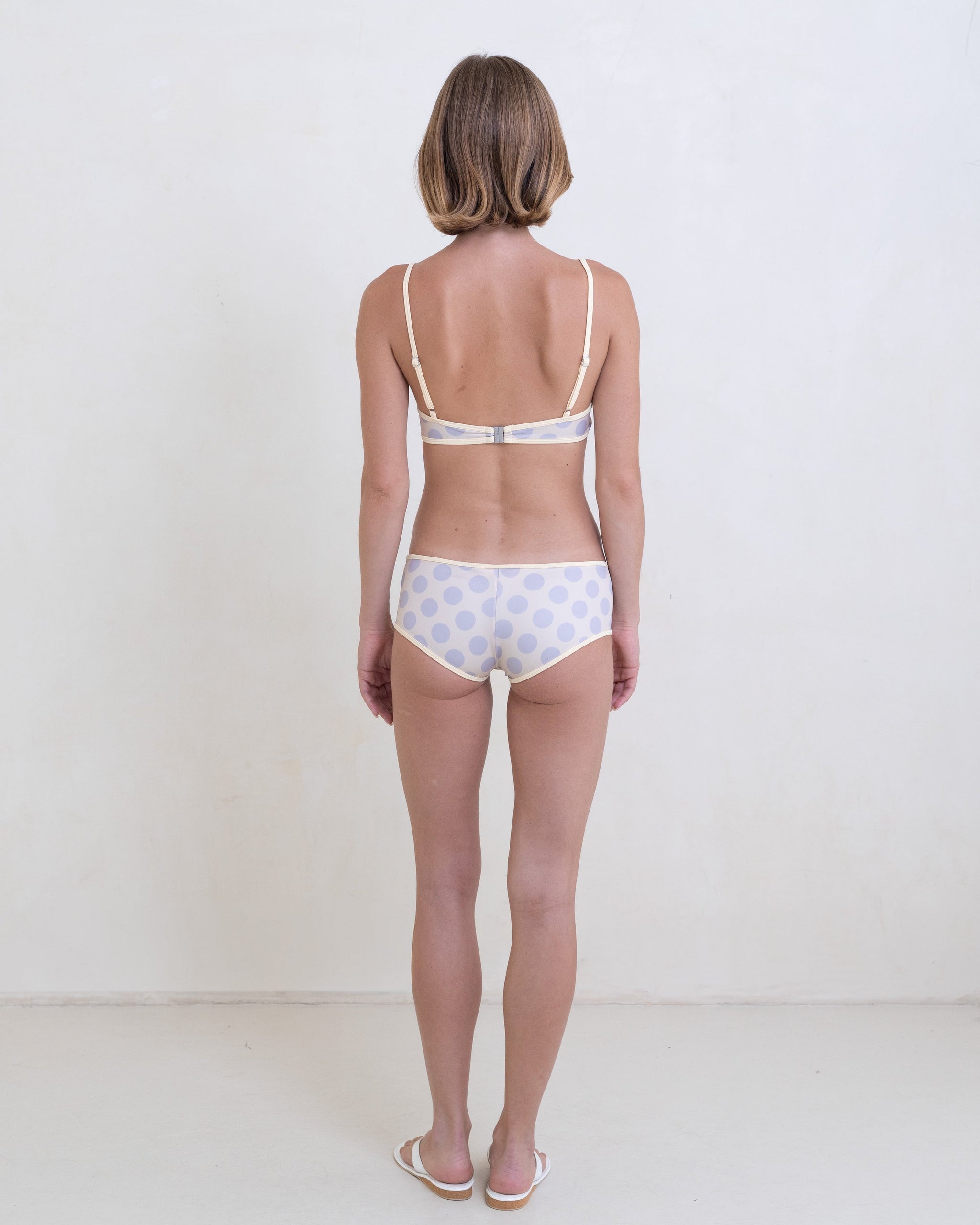 Woman wearing a gray polka dot bikini with a contrast white trim on a white background.