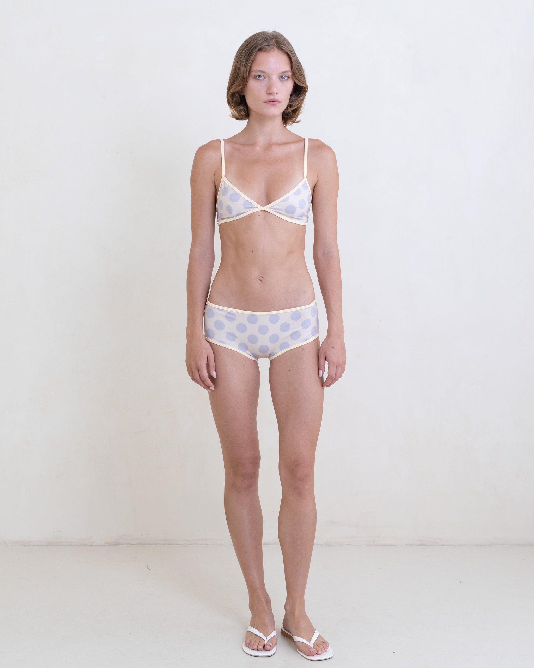 Woman wearing a gray polka dot bikini with a contrast white trim on a white background.