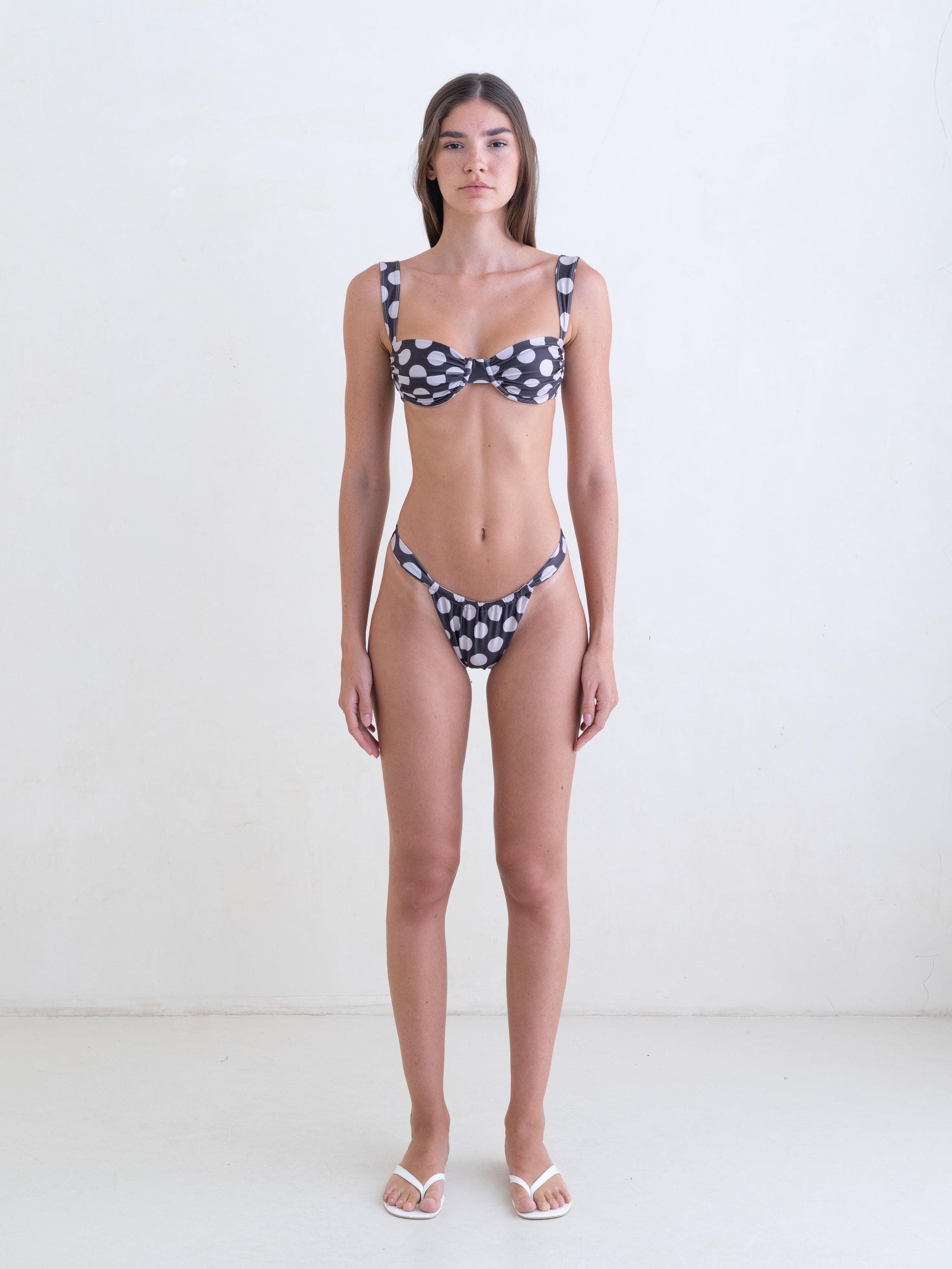 Woman wearing a white on dark brown polka dot bikini on a white background.