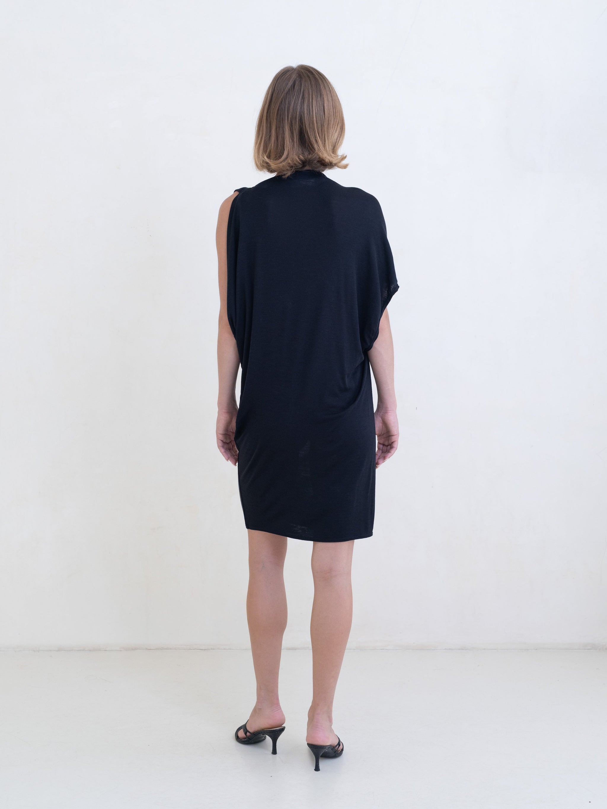 Woman wearing a black asymmetric mini dress on a white background. 