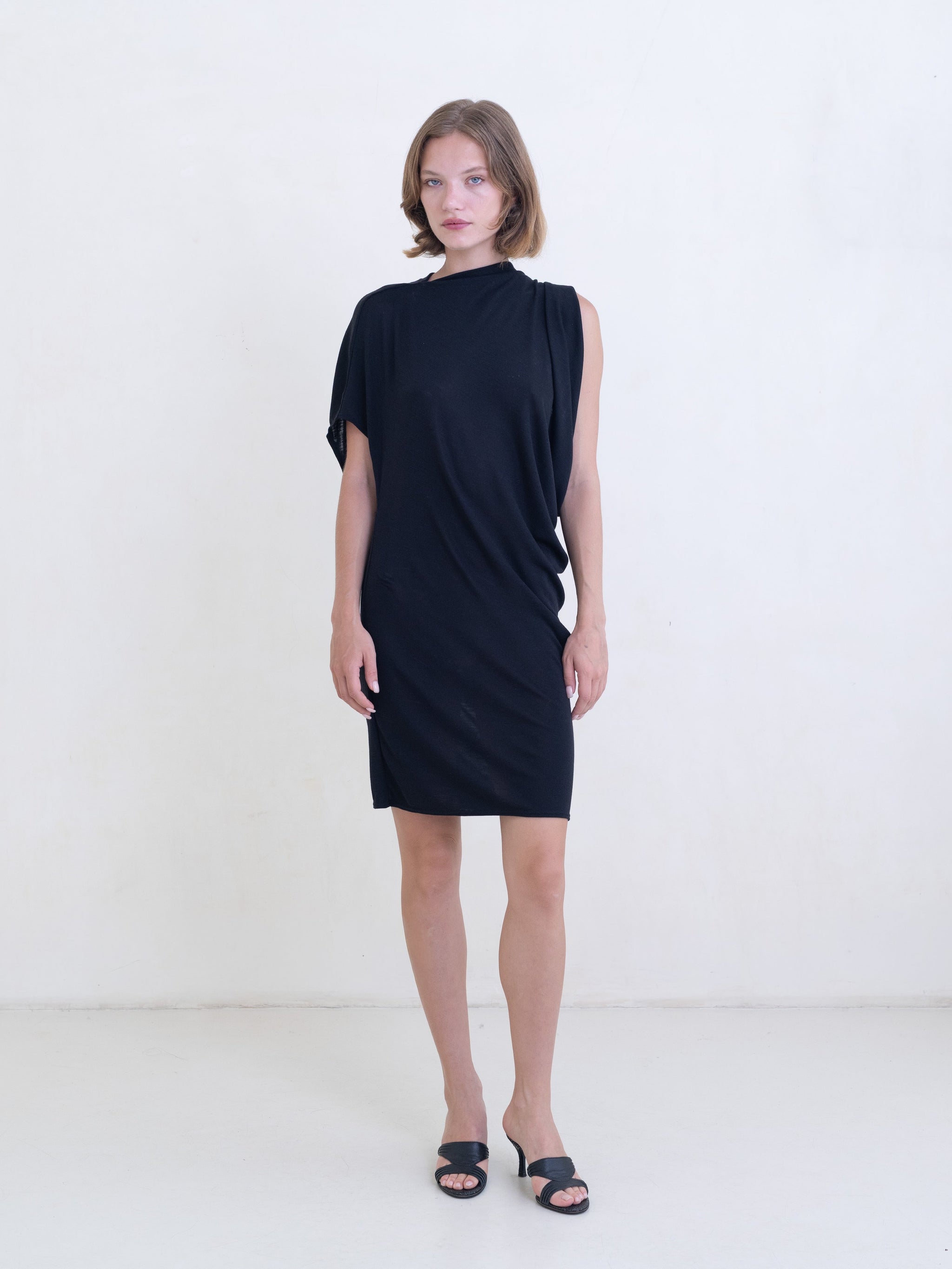 Woman wearing a black asymmetric mini dress on a white background. 