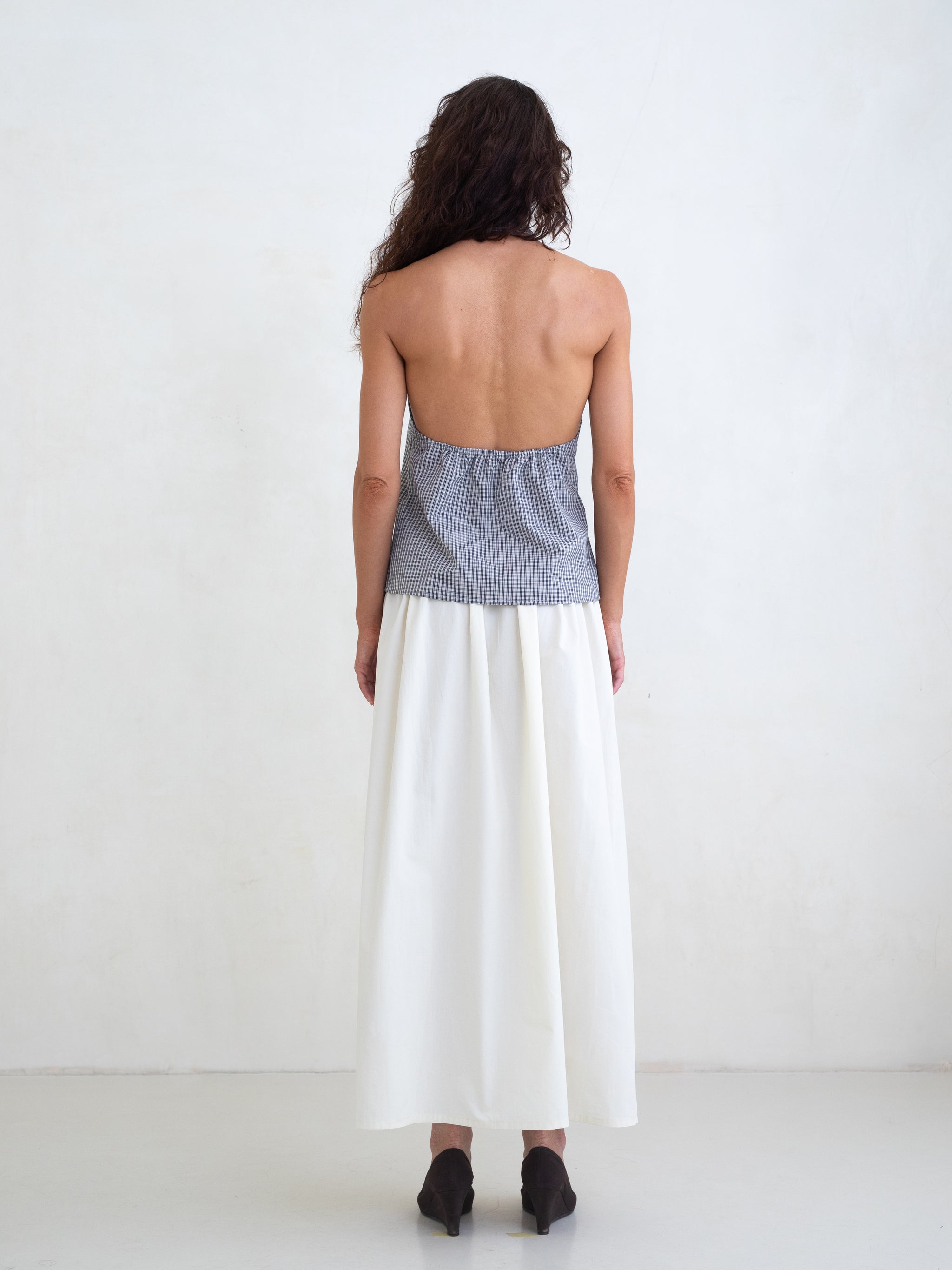 Woman wearing a black plaid v-neck halter top and an off-white maxi skirt on a white background. 