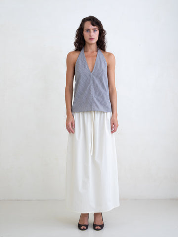 Woman wearing a black plaid v-neck halter top and an off-white maxi skirt on a white background. 