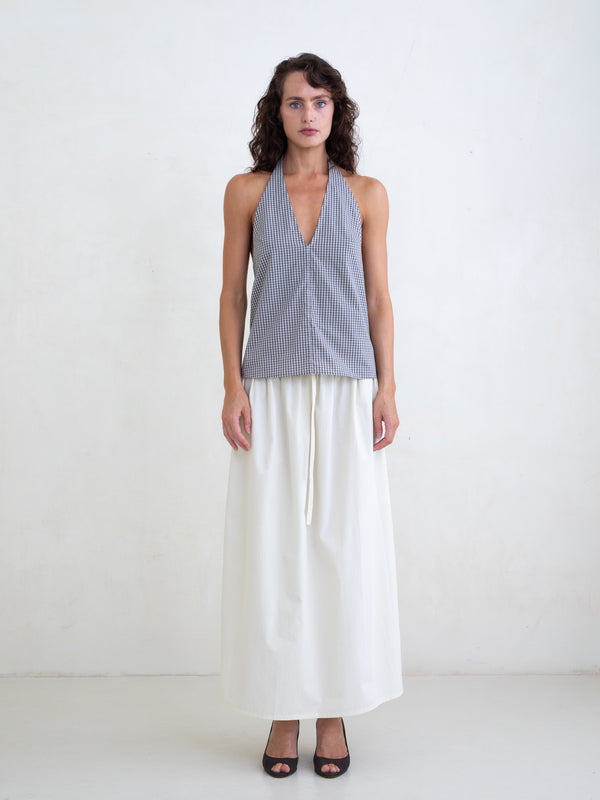 Woman wearing a black plaid v-neck halter top and an off-white maxi skirt on a white background. 