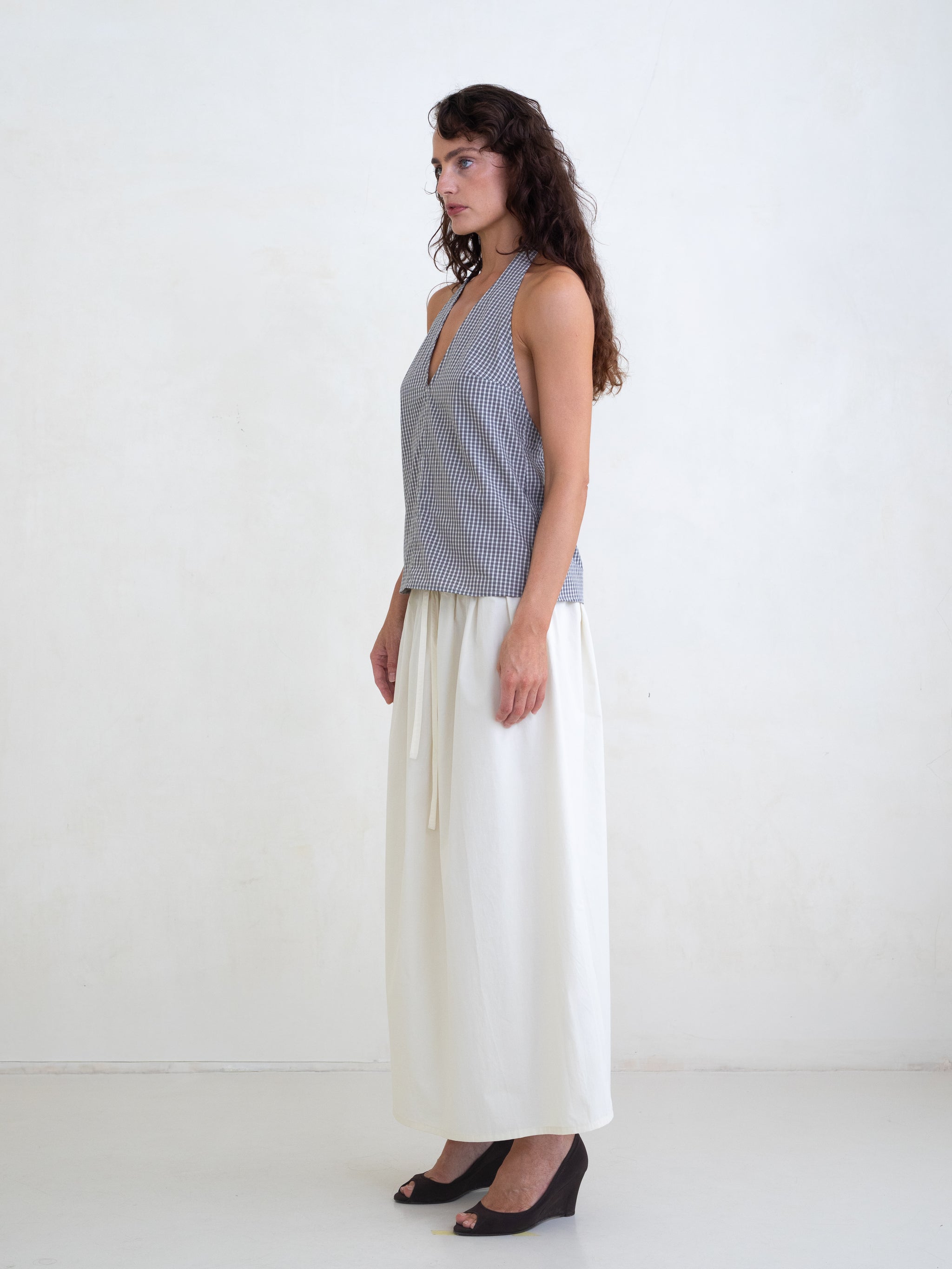 Woman wearing a black plaid v-neck halter top and an off-white maxi skirt on a white background. 