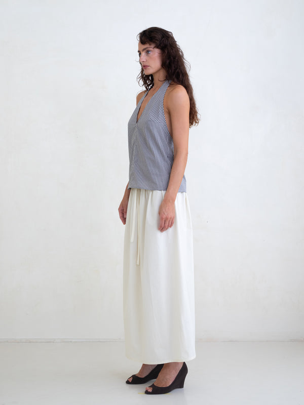 Woman wearing a black plaid v-neck halter top and an off-white maxi skirt on a white background. 