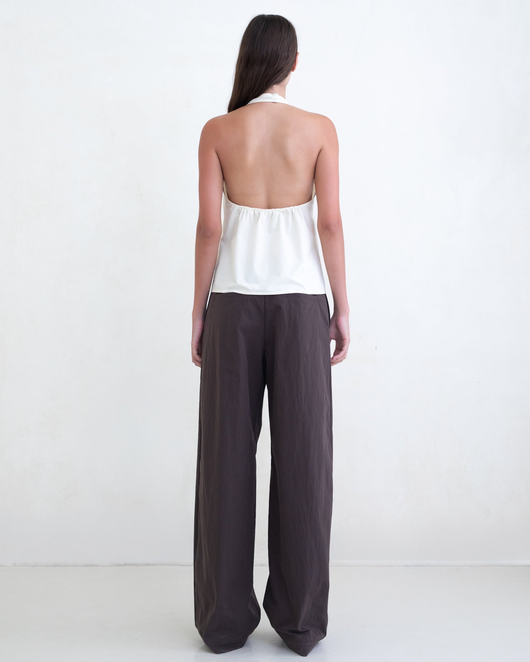 Woman wearing a cream halter top and brown wide-leg pants on a white background. 