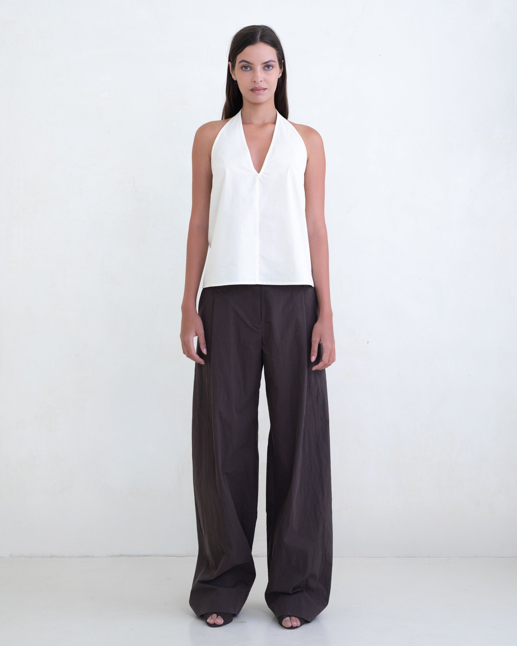 Woman wearing a cream halter top and brown wide-leg pants on a white background. 